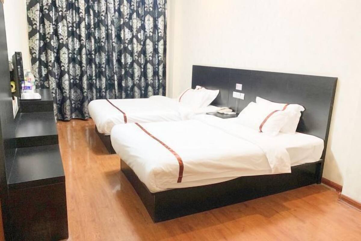 A hotel room with two beds, a wooden floor, a dark headboard, and a curtain with a pattern.