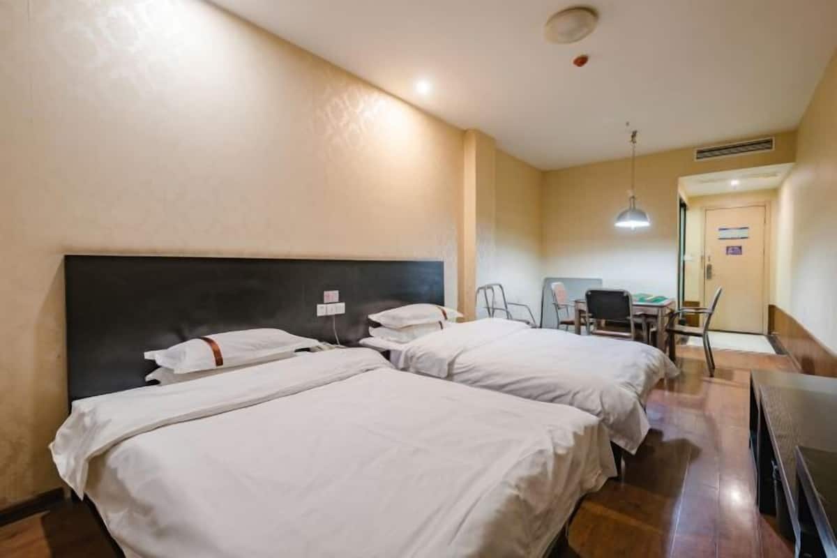 A hotel room with two beds, a desk, a chair, and a television.