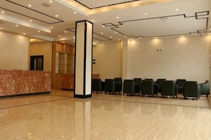 Un hall d’hôtel avec un comptoir d’accueil, une haute colonne et des rangées de chaises.