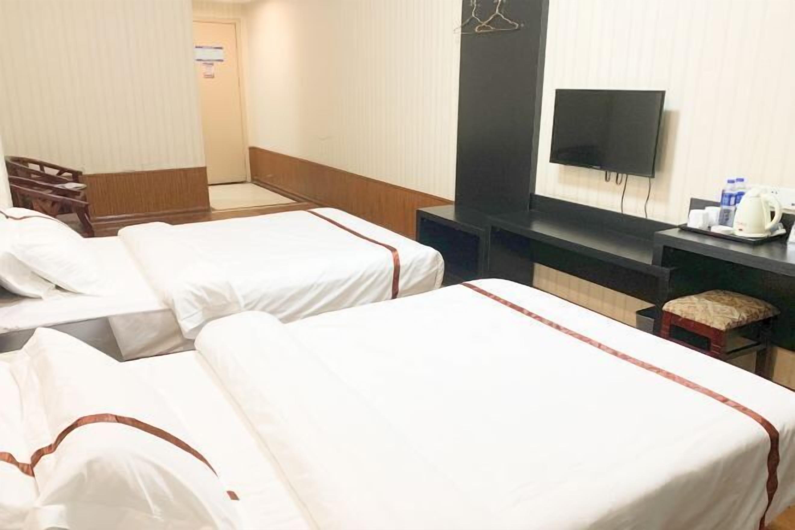 Une chambre d’hôtel avec deux lits, une télévision, un bureau avec une bouilloire et une chaise.