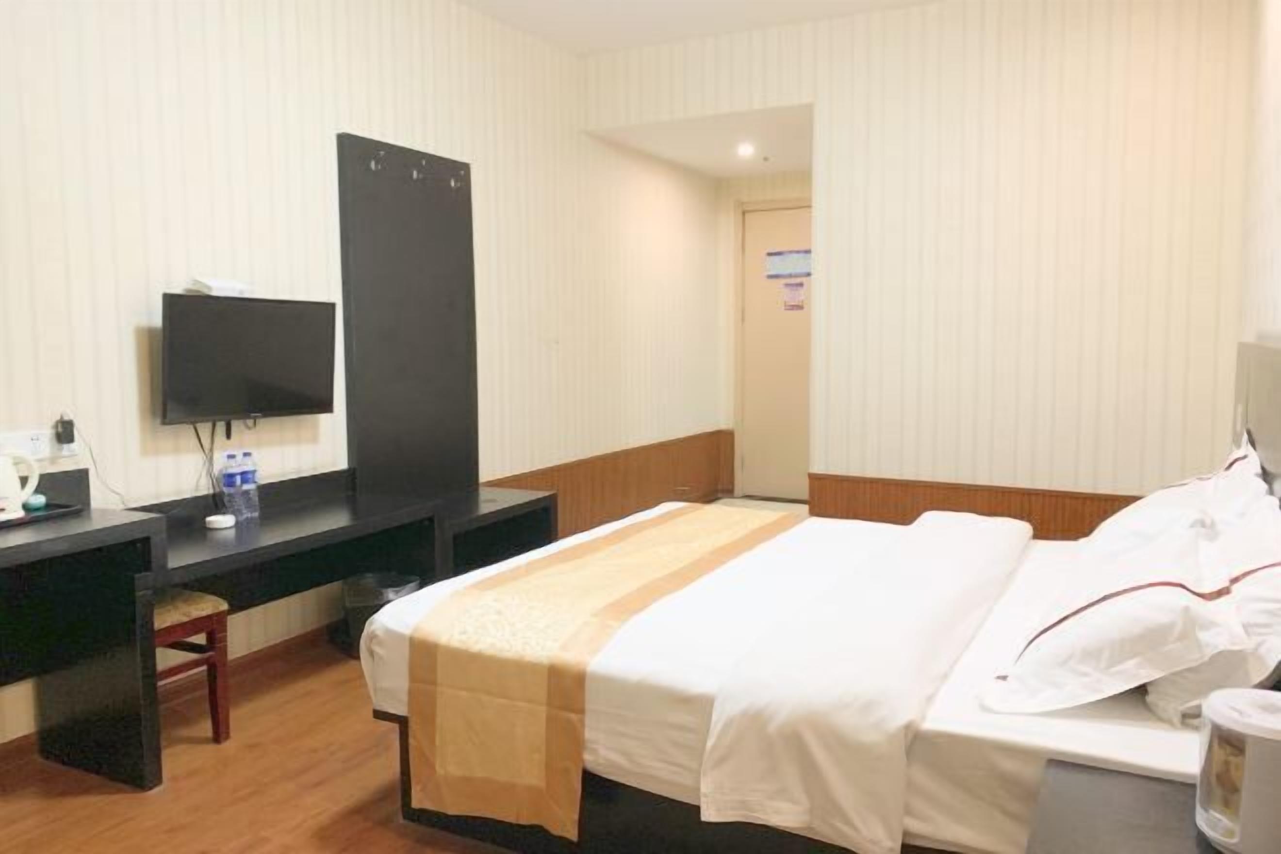 Una habitación de hotel con cama, escritorio, televisión y puerta.
