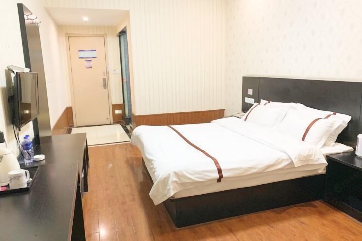 Una habitación de hotel con una cama, un escritorio, una silla, un televisor y una puerta.