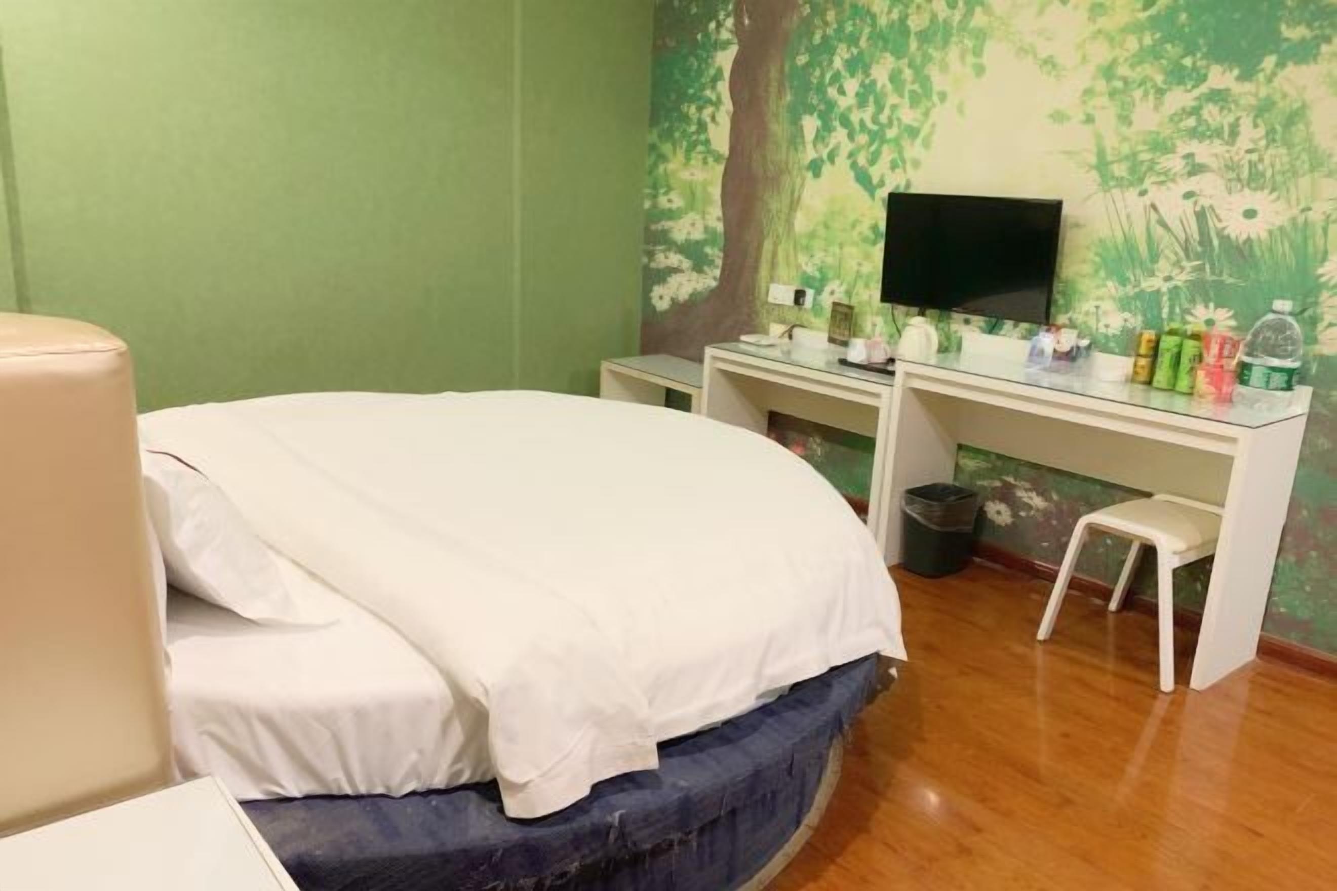 A bedroom with a bed, a desk, a television, and a small stool.