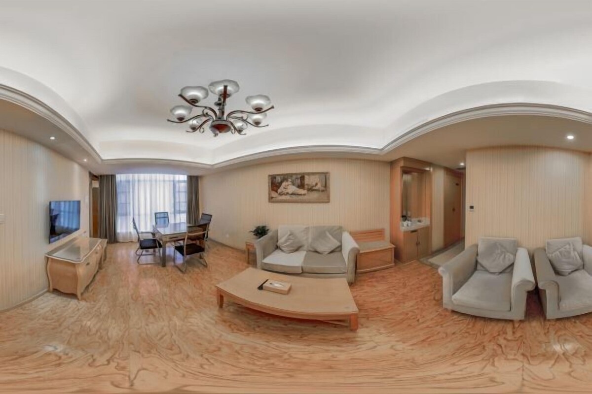 A spacious living room with a curved ceiling, a central coffee table, a sofa, and armchairs. There is a television mounted on the wall and a painting above the sofa.