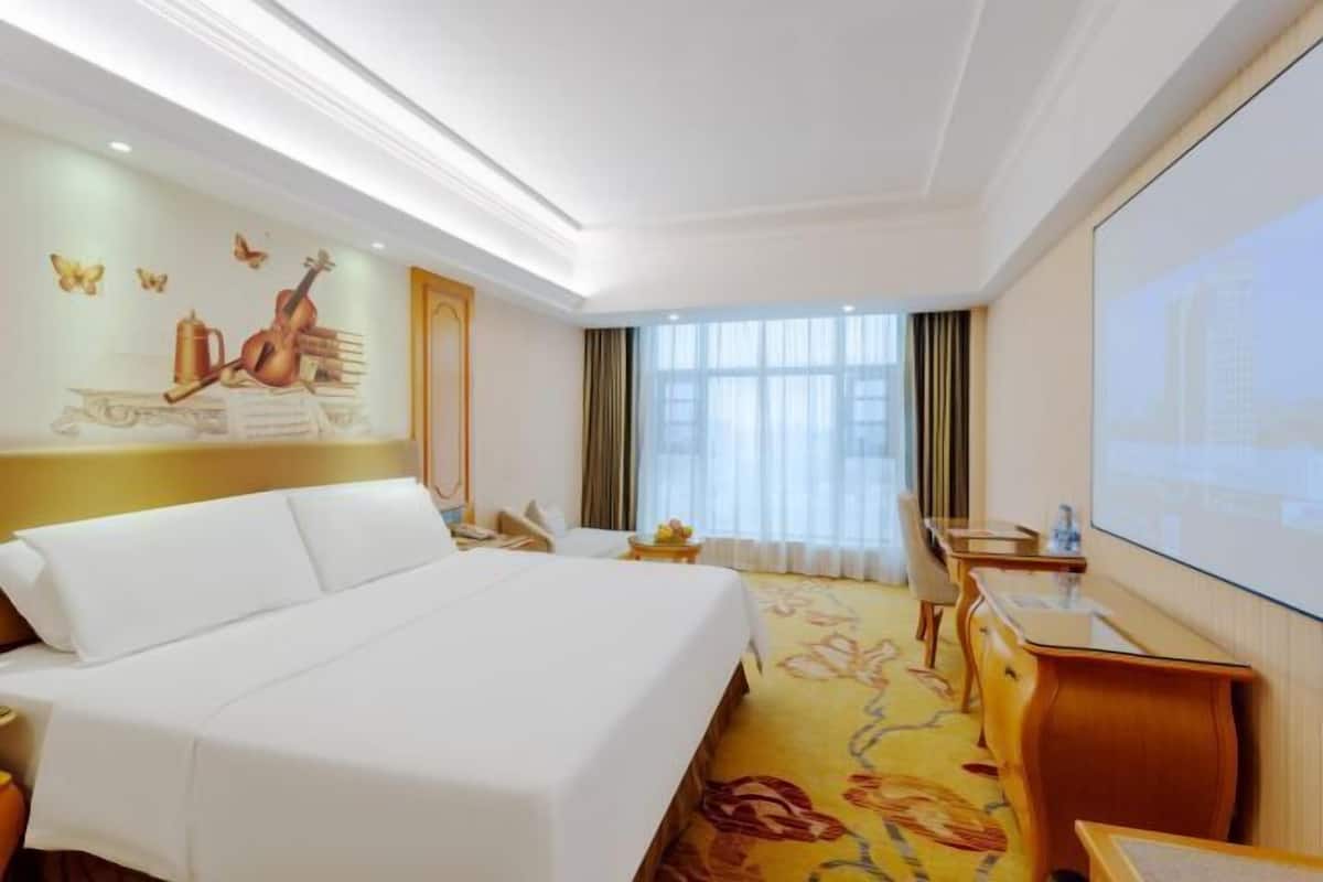 A hotel room with a bed, a desk, a chair, a television, and a window with curtains.