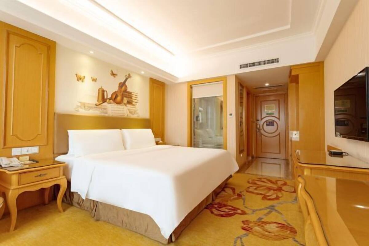 A hotel room with a large bed, wooden furniture, a television, and a floral carpet.
