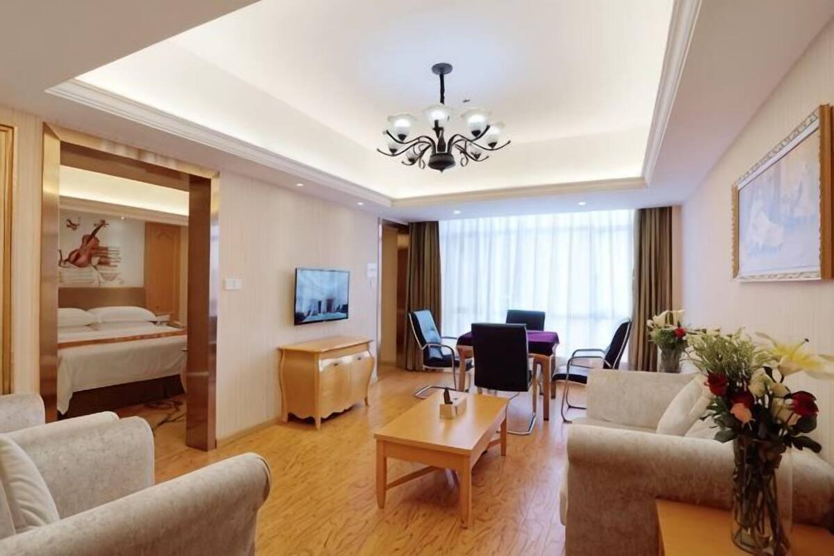 A hotel room with a bed, a desk, a chair, a TV, and a dining area.