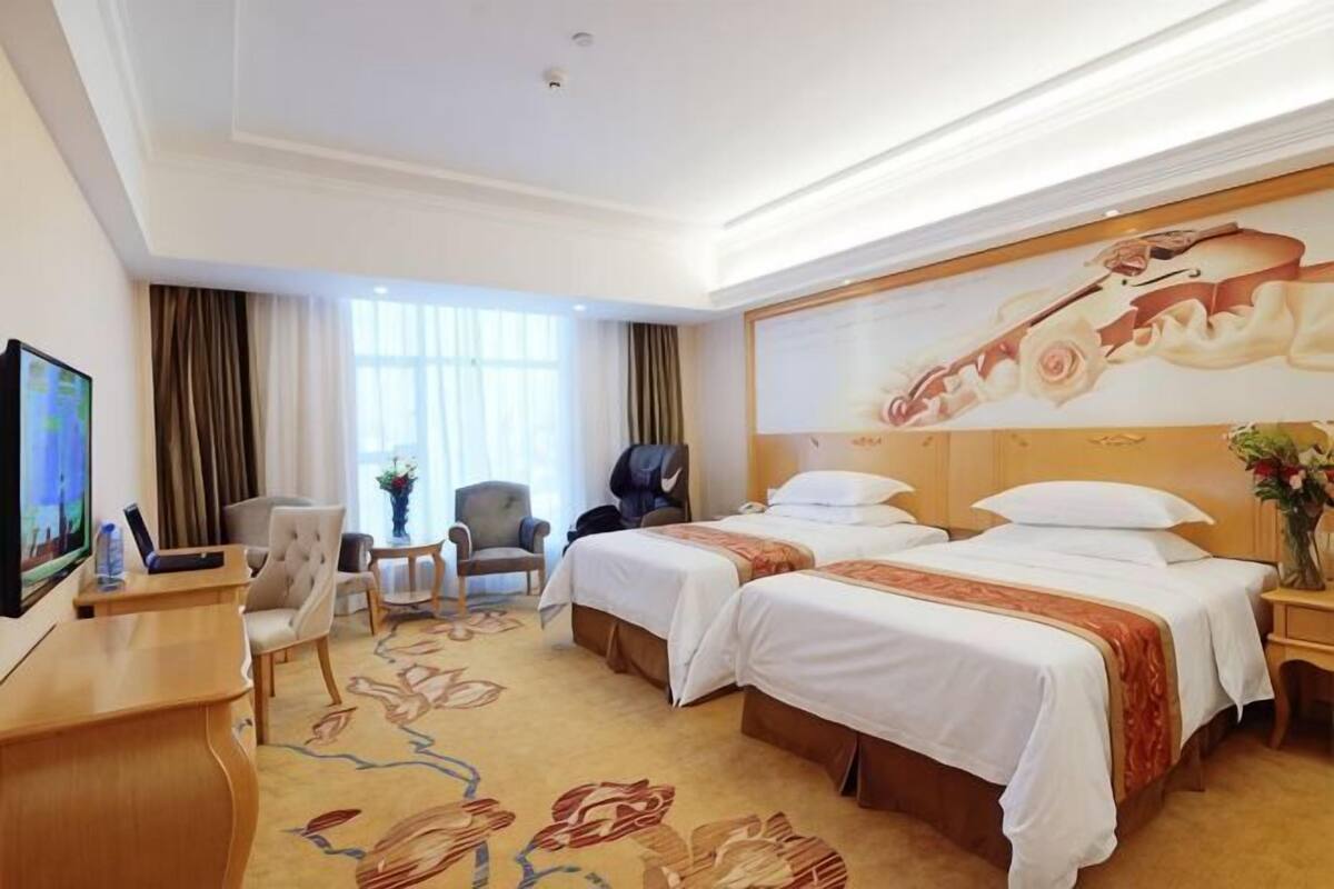 A hotel room with two beds, a desk, a TV, and a large floral mural on the wall.