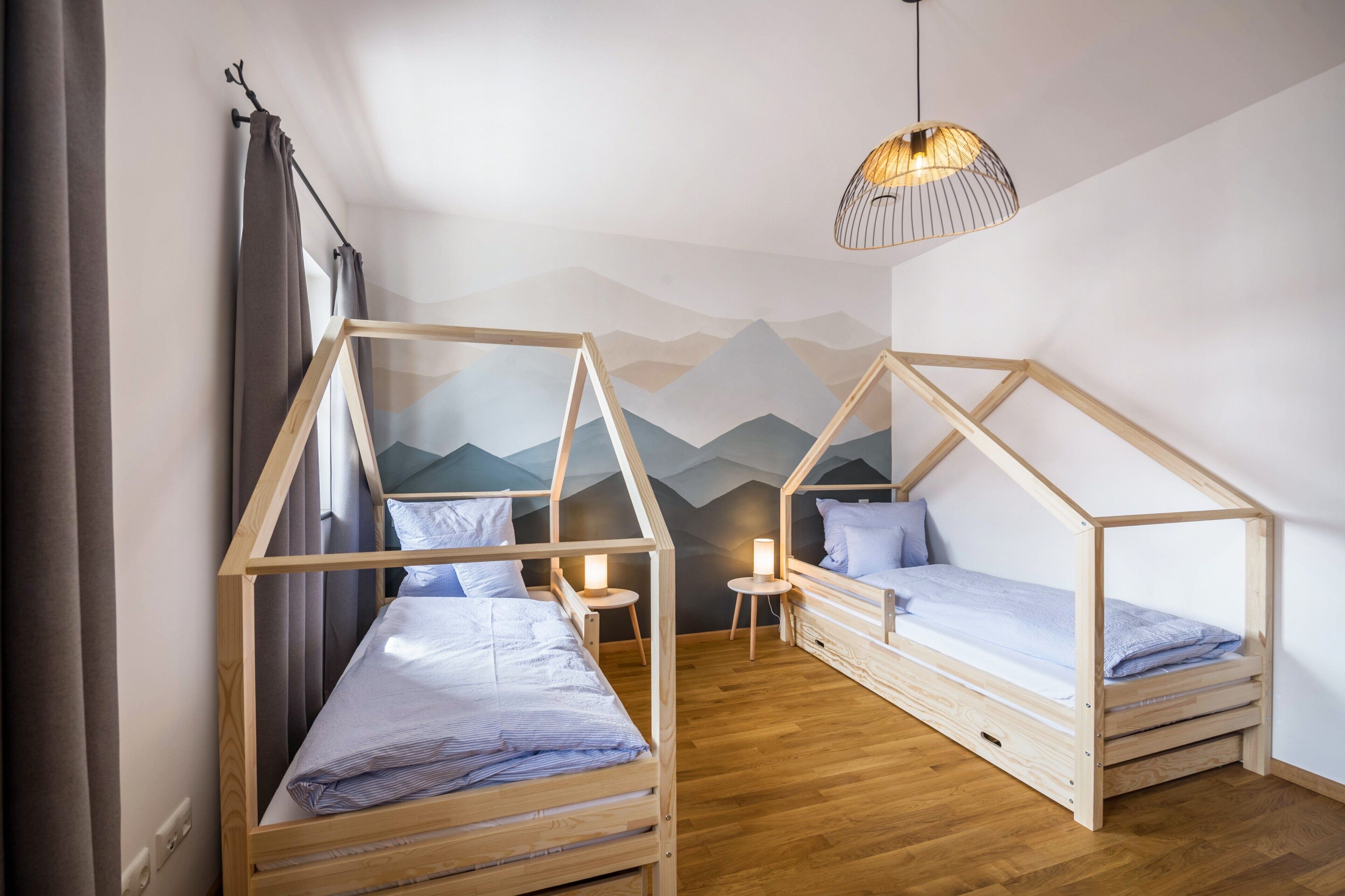 Ein Schlafzimmer mit zwei Holzbettställen, einem kleinen Nachttisch mit Lampe und einer Wandmalerei von Bergen.