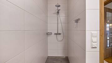 Douche met een handdouche en een wandmengkraan, betegelde wanden en een houten vloer.