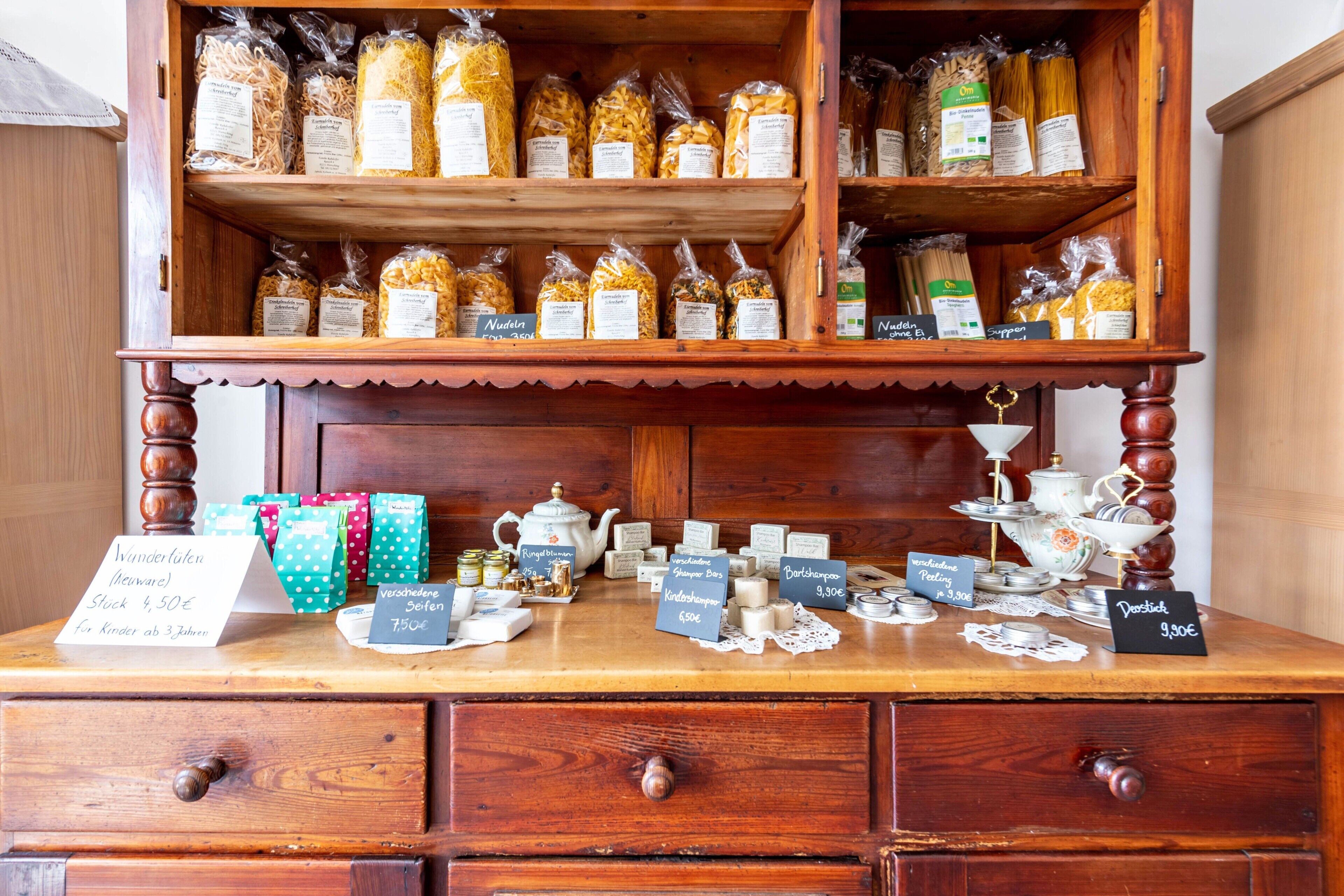 Une vitrine en bois contenant des pâtes et des condiments, une enseigne pour le chocolat Kinder, et une théière.