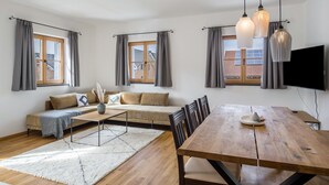Een moderne woonkamer met een bank, eettafel en grote ramen.