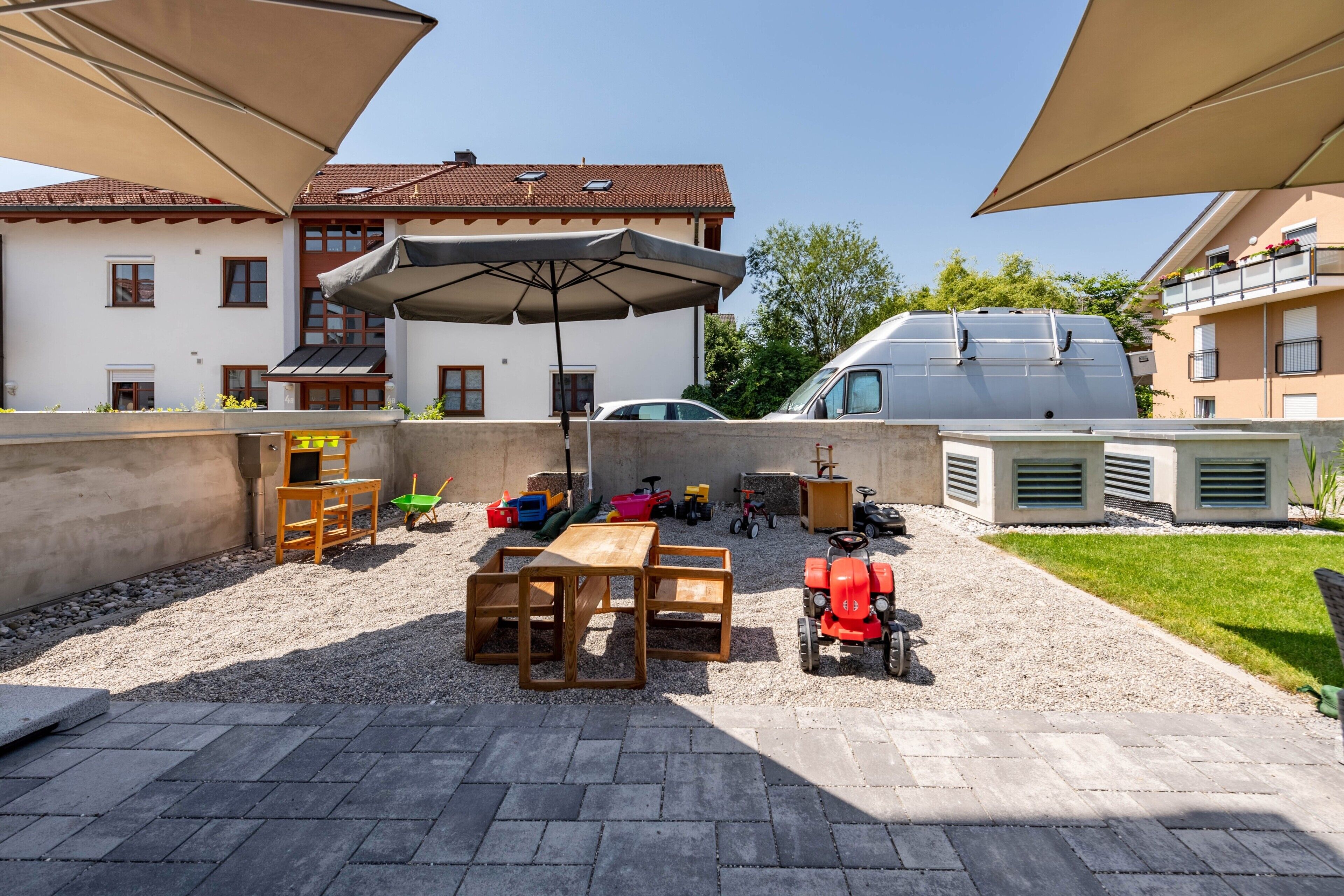 Eine Terrasse mit Tisch und Stühlen, ein roter Traktor und ein weißer Lieferwagen.