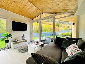 Ein modernes Wohnzimmer mit großem Fenster, Flachbildfernseher und einer Couch mit Zierkissen.