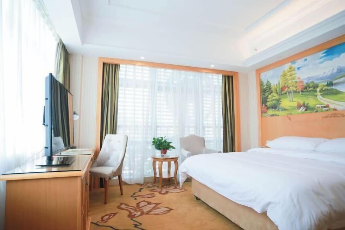 Ein Hotelzimmer mit Bett, Schreibtisch, Stuhl, Fernseher und einem Bild an der Wand.