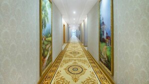 Un largo pasillo con un suelo ricamente decorado y grandes cuadros enmarcados en las paredes.