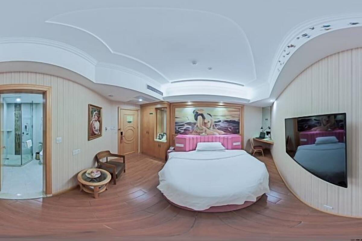 A modern hotel room with a curved ceiling, a large bed, a television, a desk, and a painting on the wall.