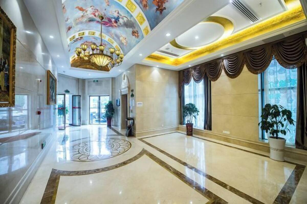 A spacious lobby with a marble floor, a large chandelier, and a mural on the ceiling.
