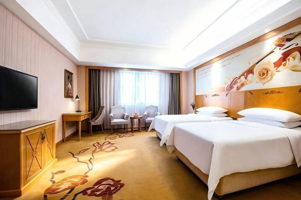 A hotel room with a TV, two beds, a desk, and a chair.