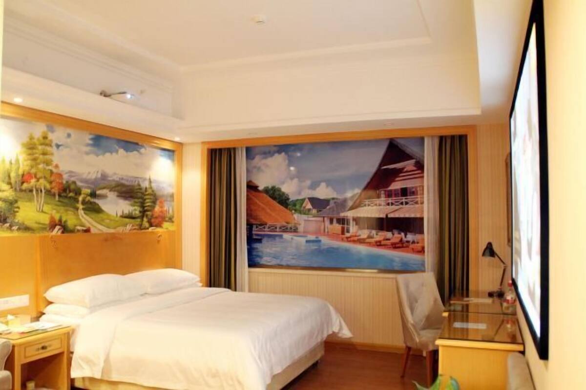 A hotel room with a bed, a desk, and a view of a mountain landscape and a swimming pool.