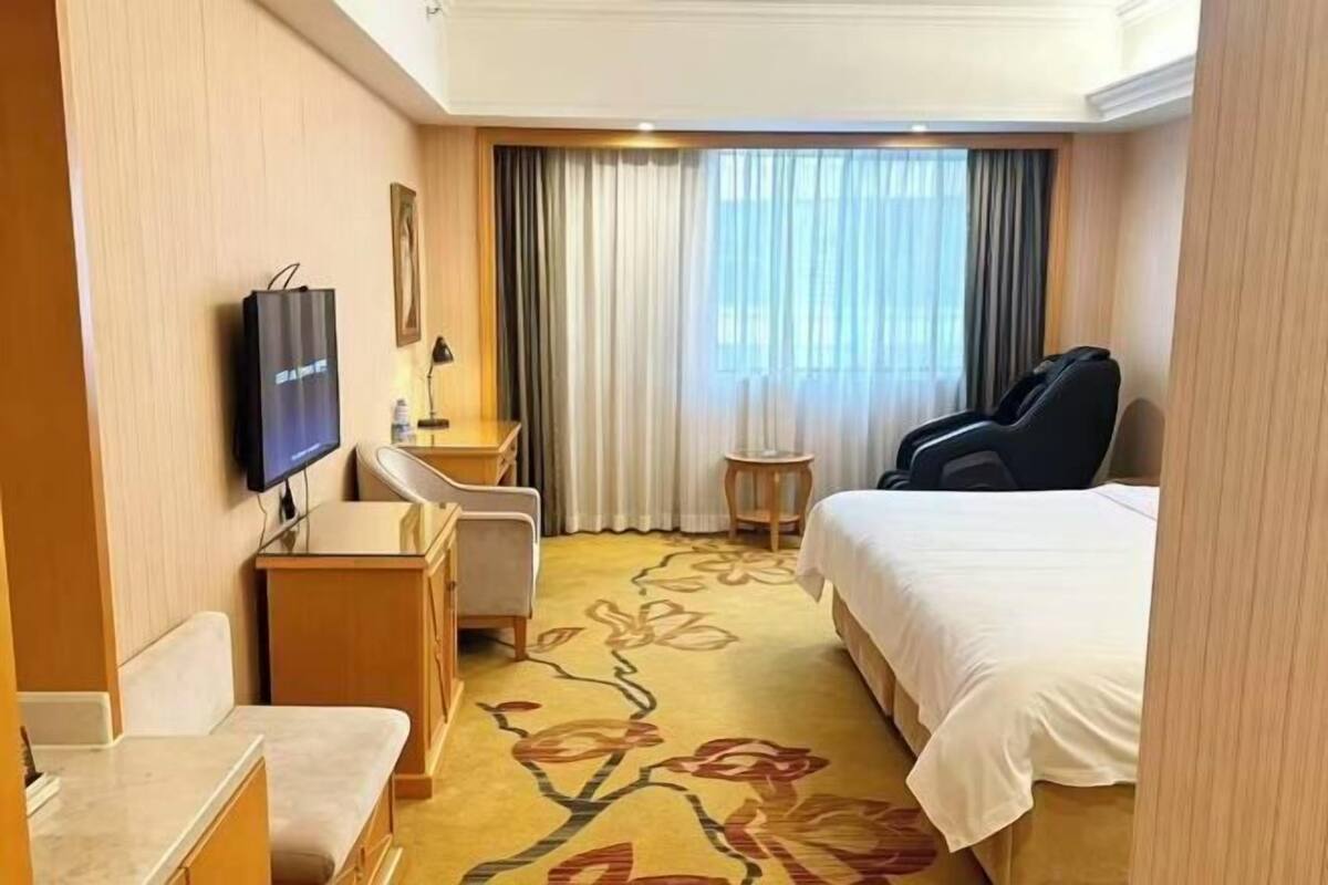 A hotel room with a bed, a desk, a chair, a TV, and a window with curtains.