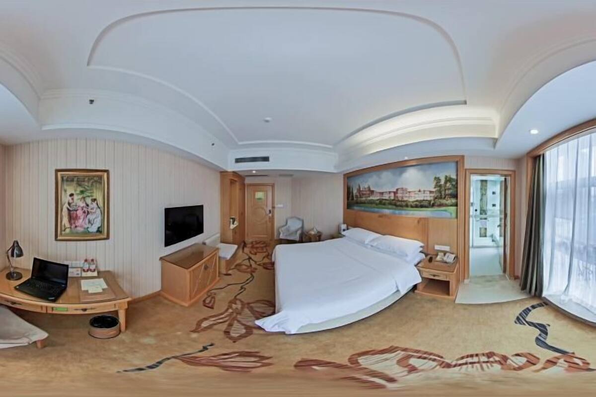 A hotel room with a bed, desk, TV, and a painting on the wall.