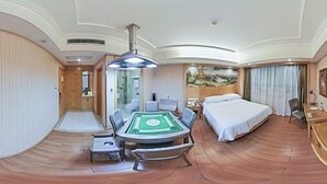 Habitación de hotel con cama, escritorio, silla, una mesa con un juego de cartas verdes y un cuadro en la pared.