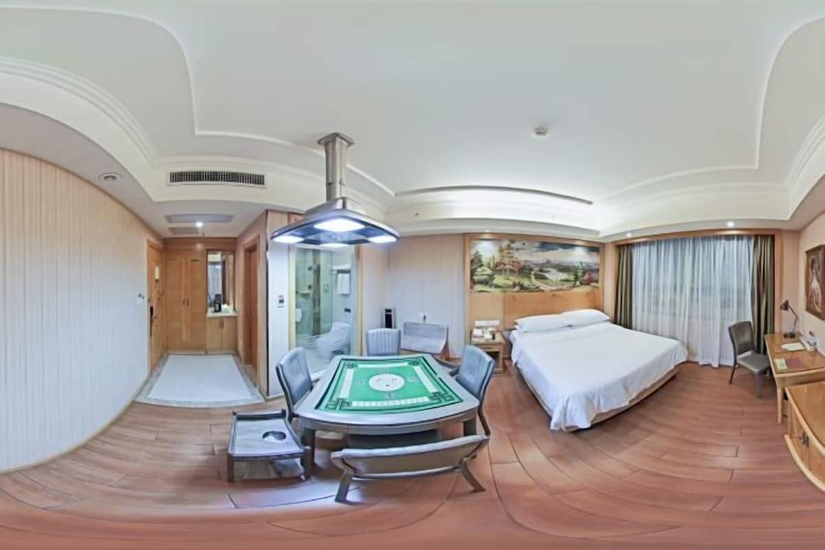 A hotel room with a bed, a desk, a chair, a table with a green playing card game, and a painting on the wall.