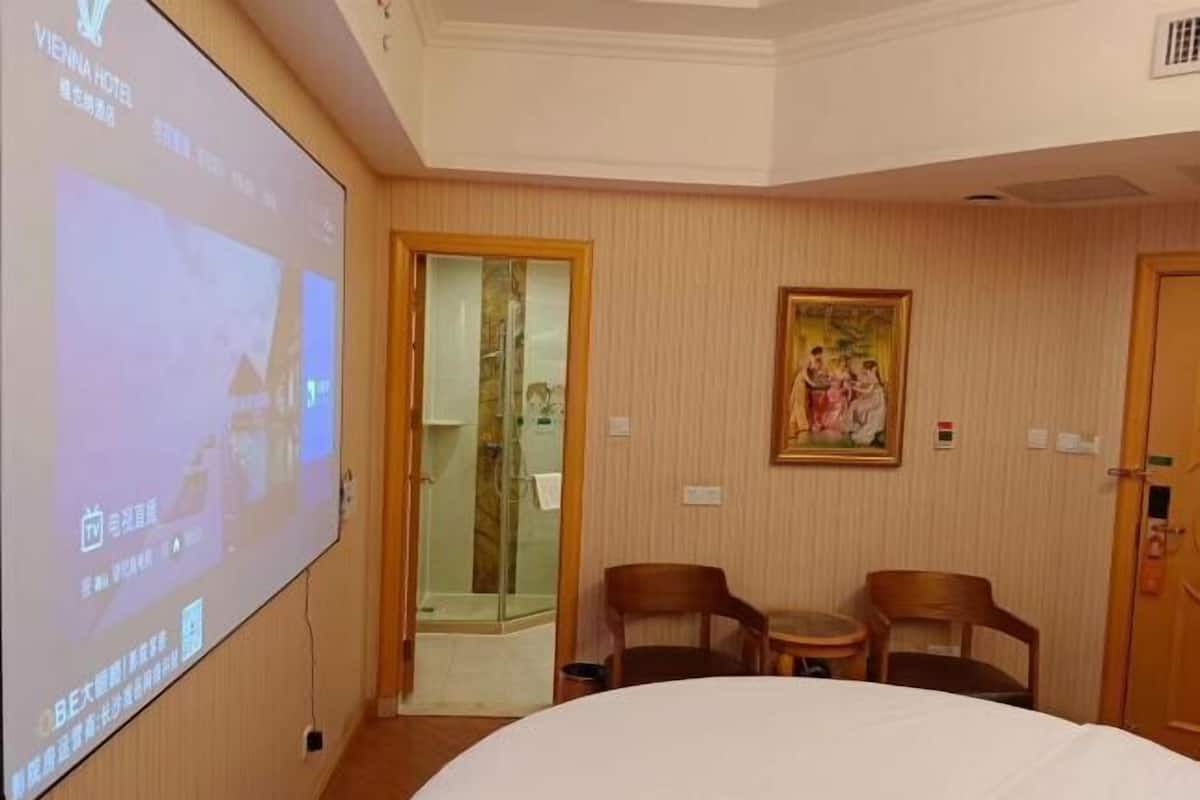 A hotel room with a bed, a TV screen, a painting, and a door.
