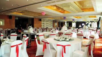 A banquet hall with round tables, white chairs, and red sashes.