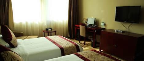 A hotel room with two beds, a desk with a computer, a television, and a small table with a water bottle.
