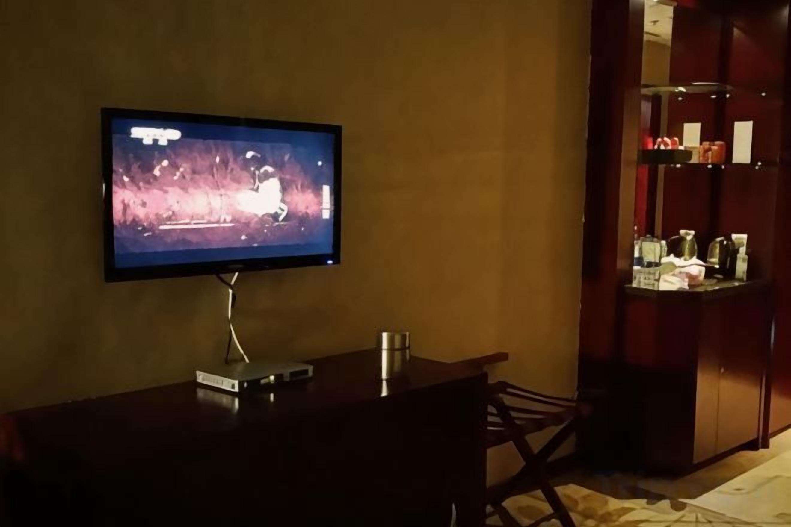 Un televisor montado en la pared, una mesita con un control remoto y una zona de bar con estantes.