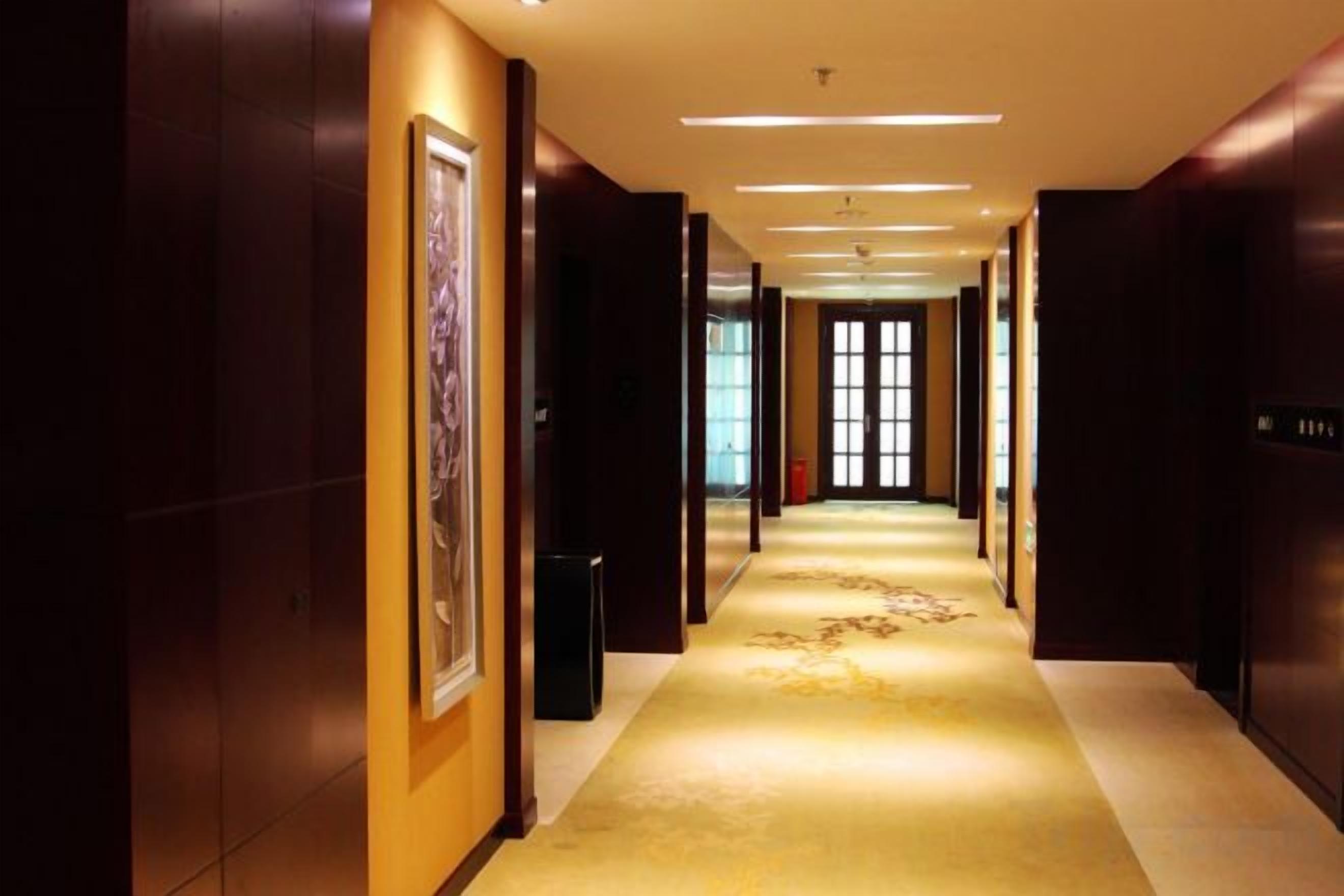 Un pasillo de hotel con piso alfombrado, obras de arte en las paredes y una puerta al final.