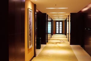 A hotel hallway with a carpeted floor, framed artwork on the walls, and a door at the end. - Donghua Hotel (Zherong)