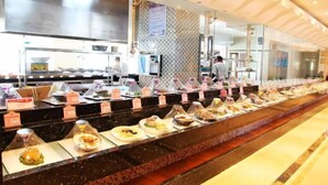 A buffet setup with various dishes displayed in clear containers, a kitchen area in the background, and a patterned wall. - Donghua Hotel (Zherong)