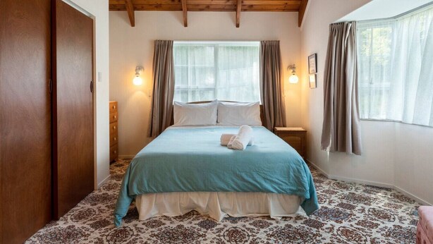 A bedroom with a wooden ceiling, a bed with a blue bedspread, two bedside lamps, a nightstand, and a patterned carpet.