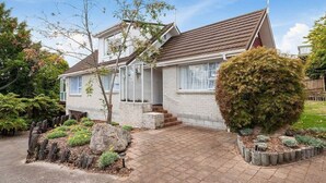 A single-story house with a tiled driveway, a small front yard with a tree and a bush, and a wooden fence.