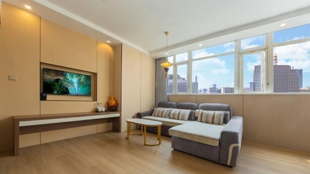 Una sala de estar moderna con un sofá, una mesa de centro, un televisor montado en la pared y un ventanal con vistas a la ciudad.