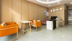 Una moderna zona de recepción con mostrador, área de estar con sillas naranjas, una pequeña mesa y un mostrador con una computadora.