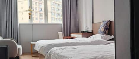 Una habitación de hotel con dos camas, una silla, una mesita y una ventana con cortinas.