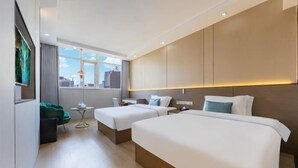 Habitación de hotel con dos camas, una mesita, una silla y vistas a la ciudad.
