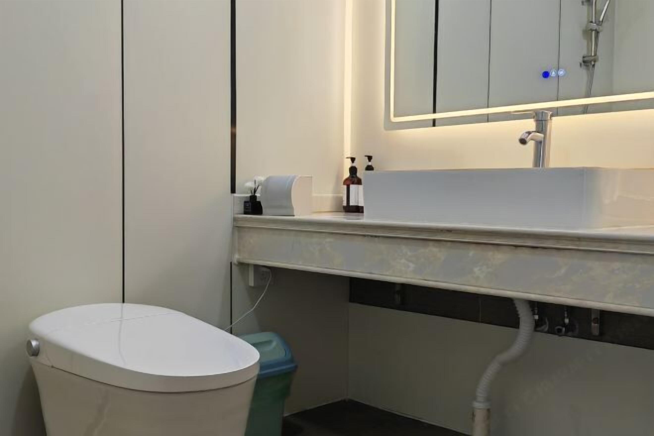 Um banheiro moderno com vaso sanitário branco, pia com espelho acima e lixeira.