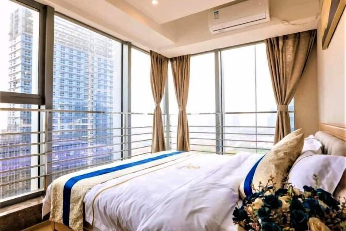 A hotel room with a large window, a bed with a blue-striped bedspread, and a view of a cityscape.