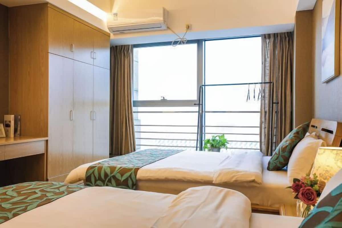 A hotel room with two beds, a wardrobe, a balcony with curtains, and a window with a view.