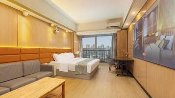A hotel room with a bed, a sofa, a small table, and a view of the city.