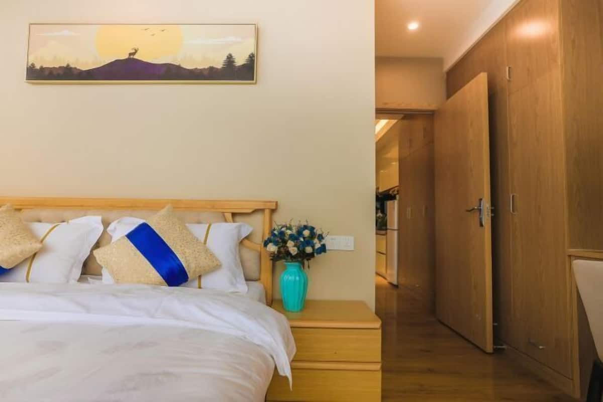 A bedroom with a bed, pillows, a vase of flowers, and a painting on the wall.