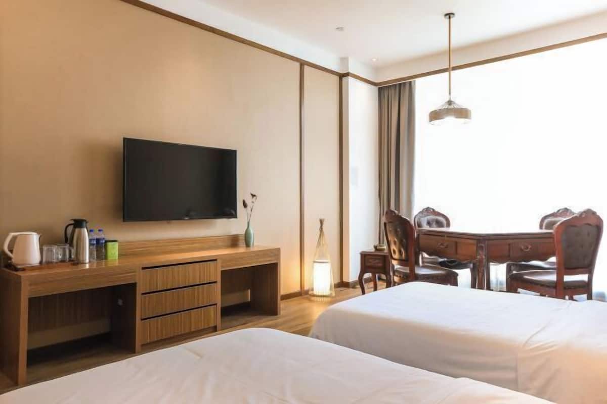 A hotel room with two beds, a TV, a wooden desk, and a dining table with chairs.