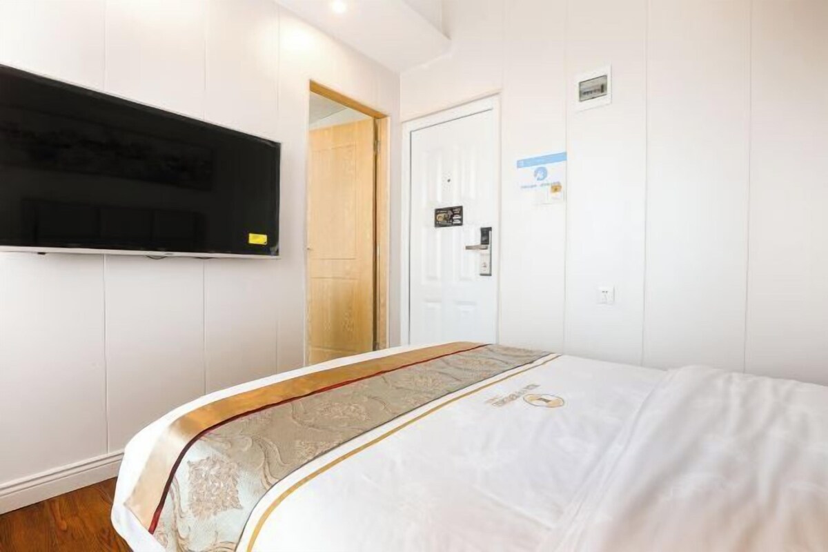 A hotel room with a bed, a television mounted on the wall, a door with a sign, and a light switch.