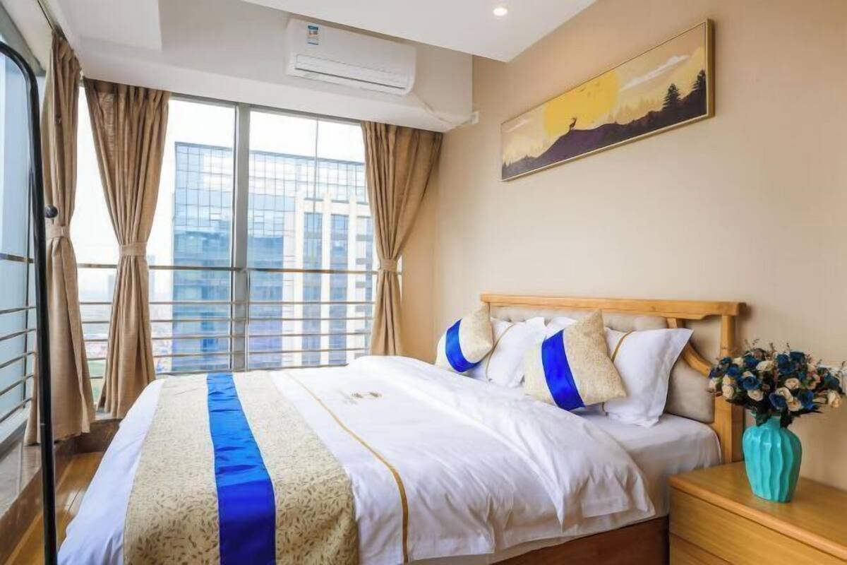 A hotel room with a large bed, a wooden headboard, a nightstand with a vase of flowers, and a painting on the wall.