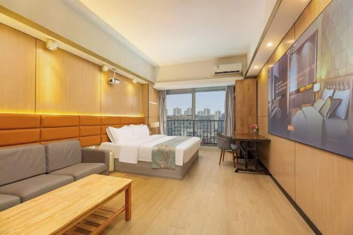A hotel room with a bed, sofa, desk, and a large window with a city view.